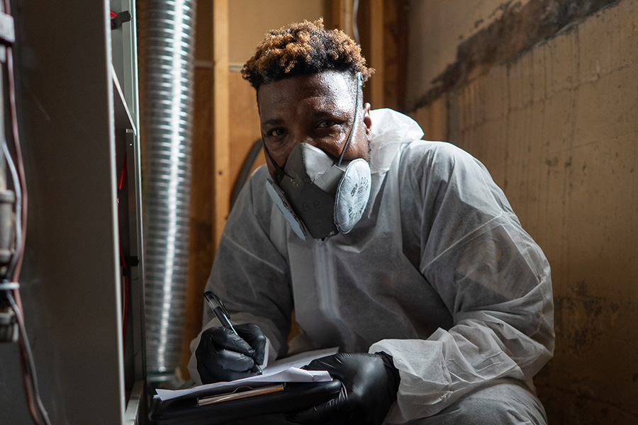 Man in protective clothes poses for the camera as he's taking notes on an HVAC unit.