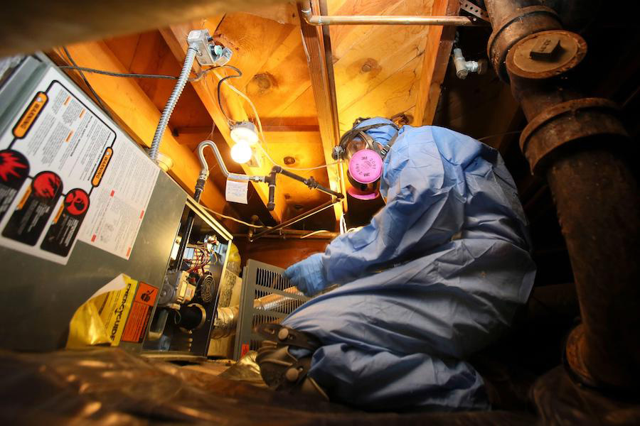 Person in a hazmat suit works on a HVAC unit.