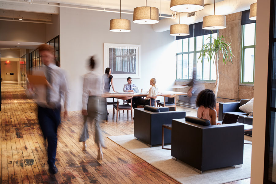 A well-lit, open office with men and women moving quickly across the space.