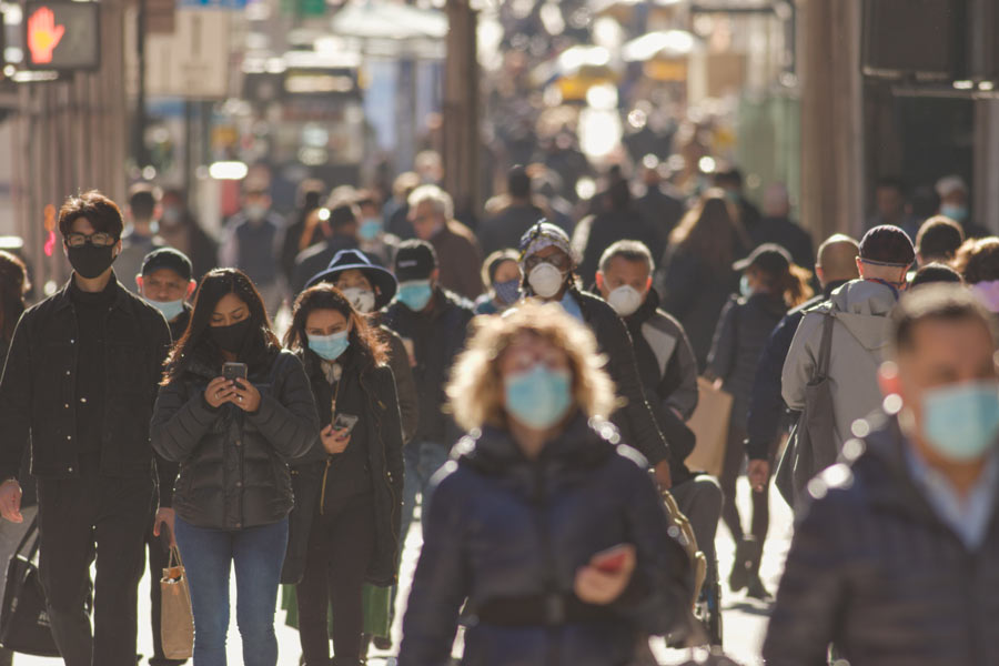 Photo of a bustling city street filled with people wearing masks.