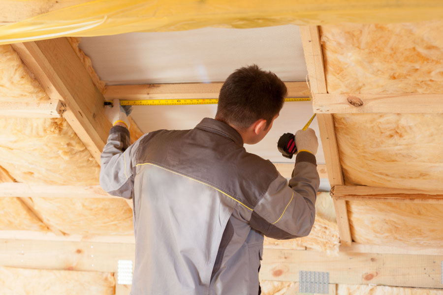 Man measures wood framing in a structure for insulation installation.