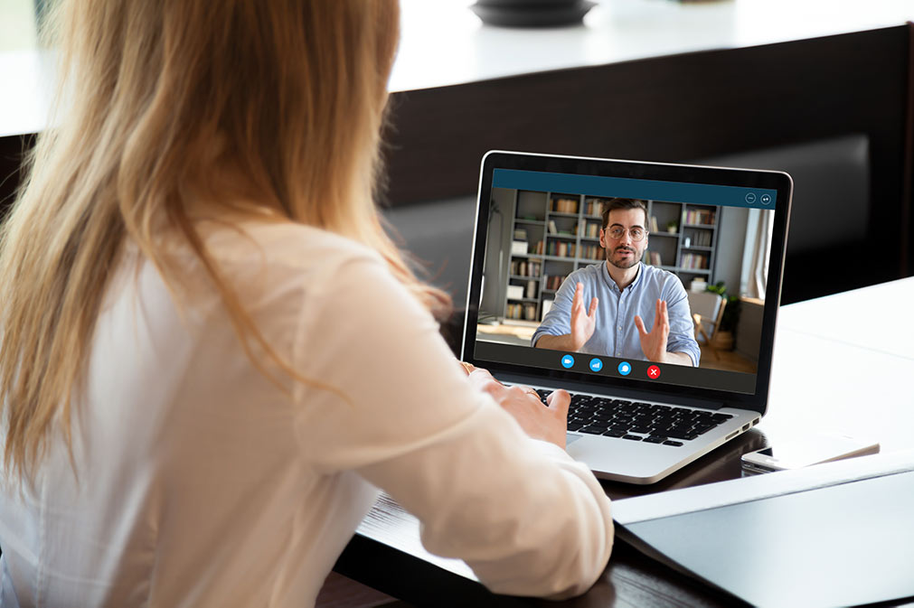 A woman using a laptop. On screen is a video call with a man talking