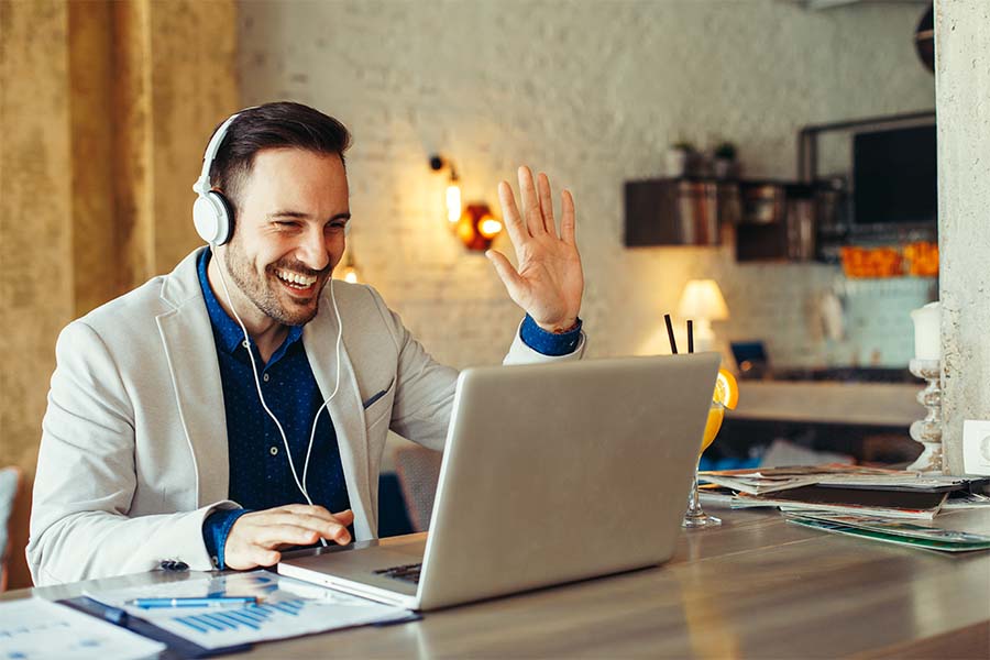 Man with headphones on waving at his computer.