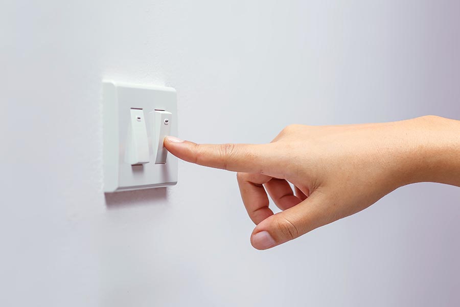 Photo of a person's hand turning off a light switch.