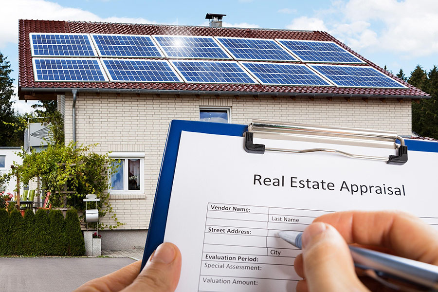 Photo with a clipboard in the foreground reading, "Real Estate Appraisal" and a house will solar panels on the roof in the background.