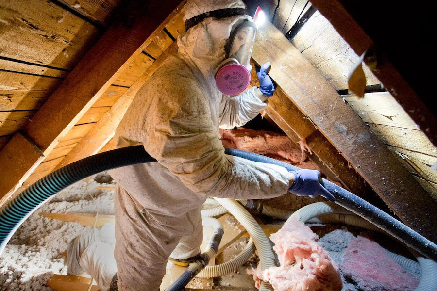 Worker in hazmat suit in an attic using a device to fix insultation