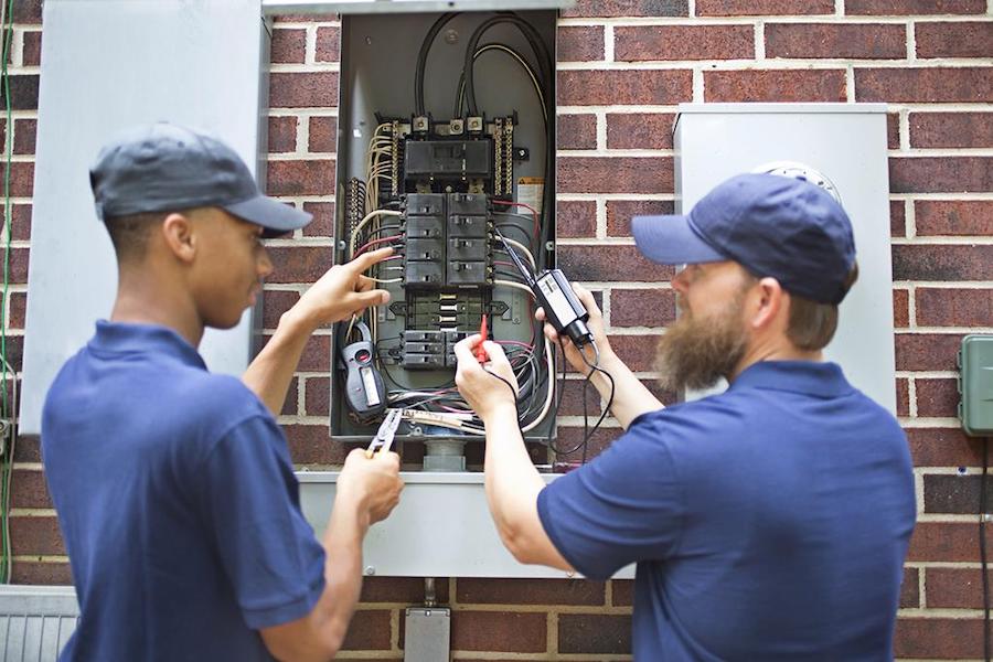 Two people working together and training on an electrical box.