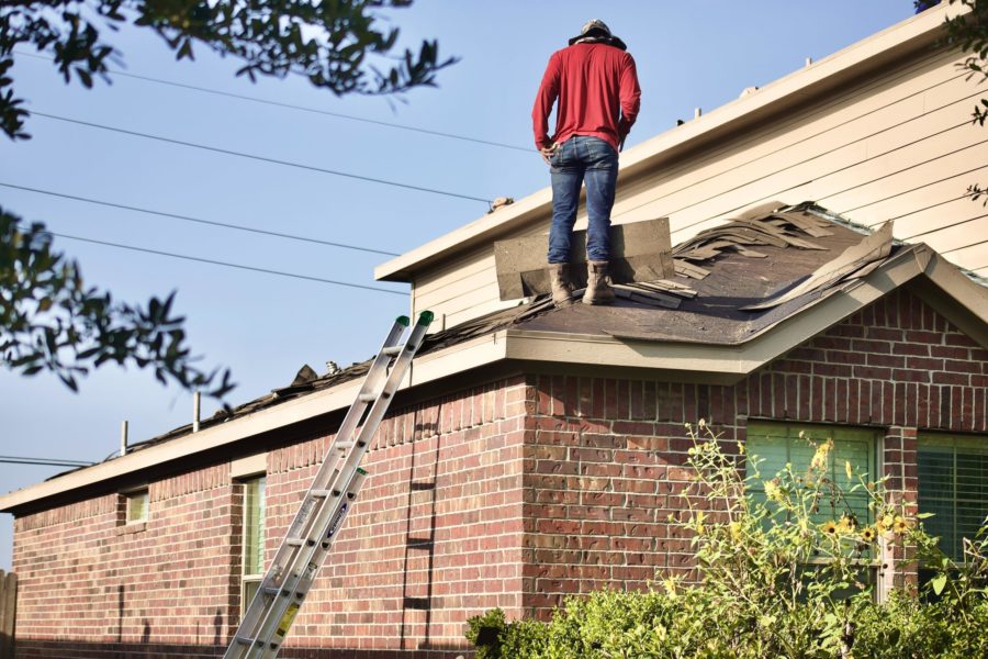 Man uses a ladder to climb on roof of home to replace the shingles.