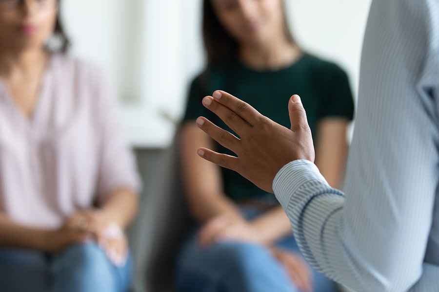 A photo of a meeting with people blurred and a hand in focus.