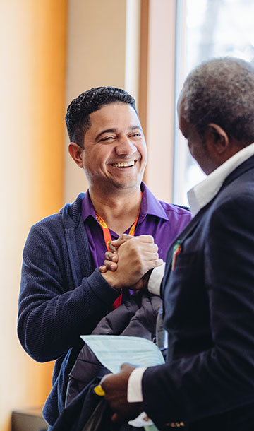 Two mean smiling and shaking hands at a BPA conference event.