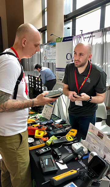 Events4-HPC2019-360x610 Two men at a table of weatherization tools discussing them at a tradeshow.
