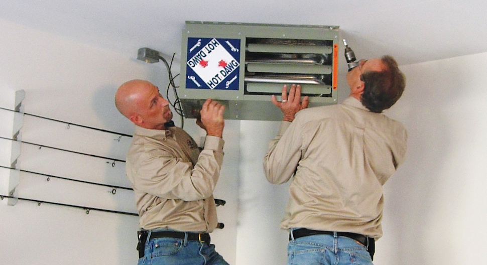 Two individuals in matching shirts and jeans installing a heating system on a ceiling