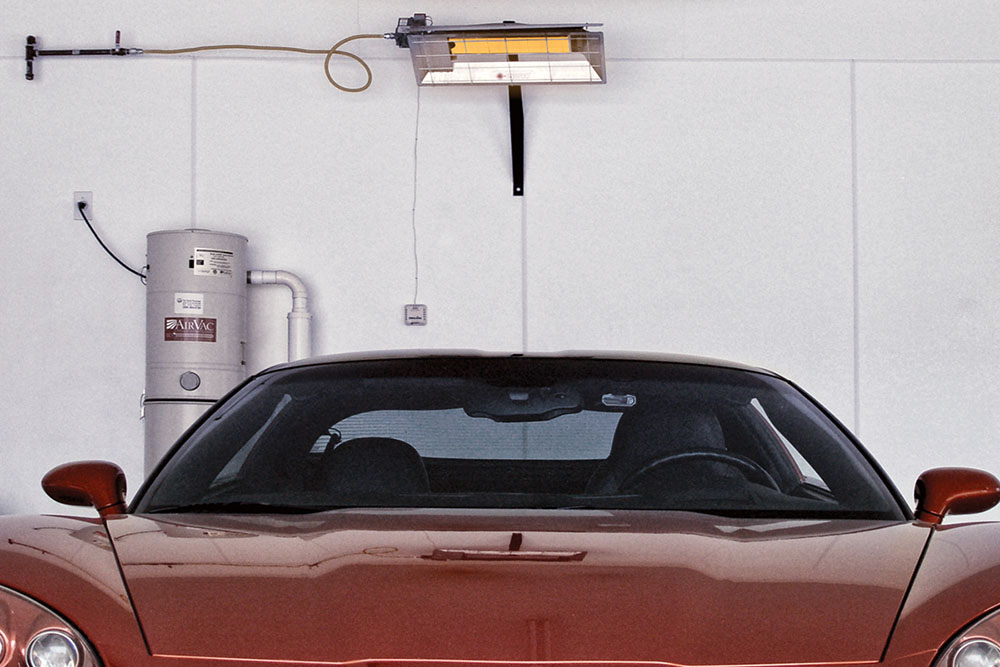 A car parked in a garage with an overhead heating system glowing orange, signifying it is on