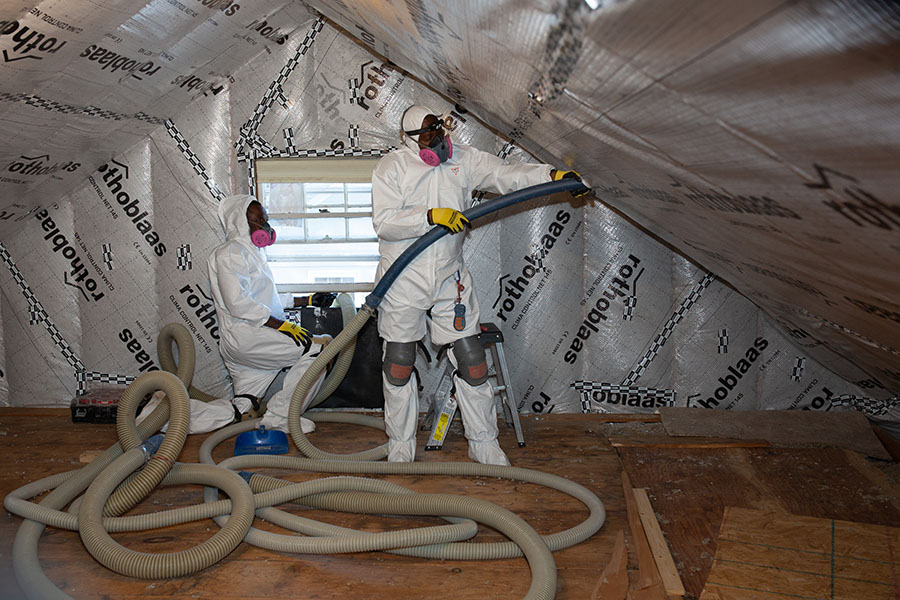 Two home performance workers in an attic adding insulation.