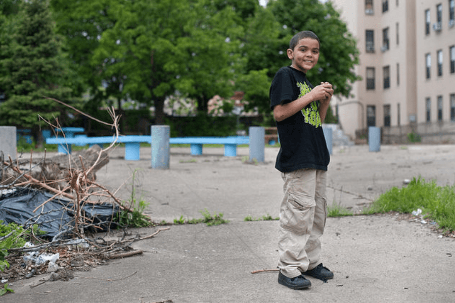 Boy in the Bronx standing outside building smiling