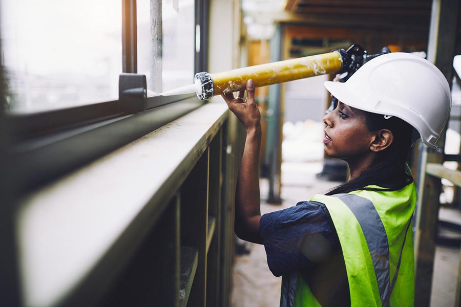 Female construction worker in protective gear applies caulk