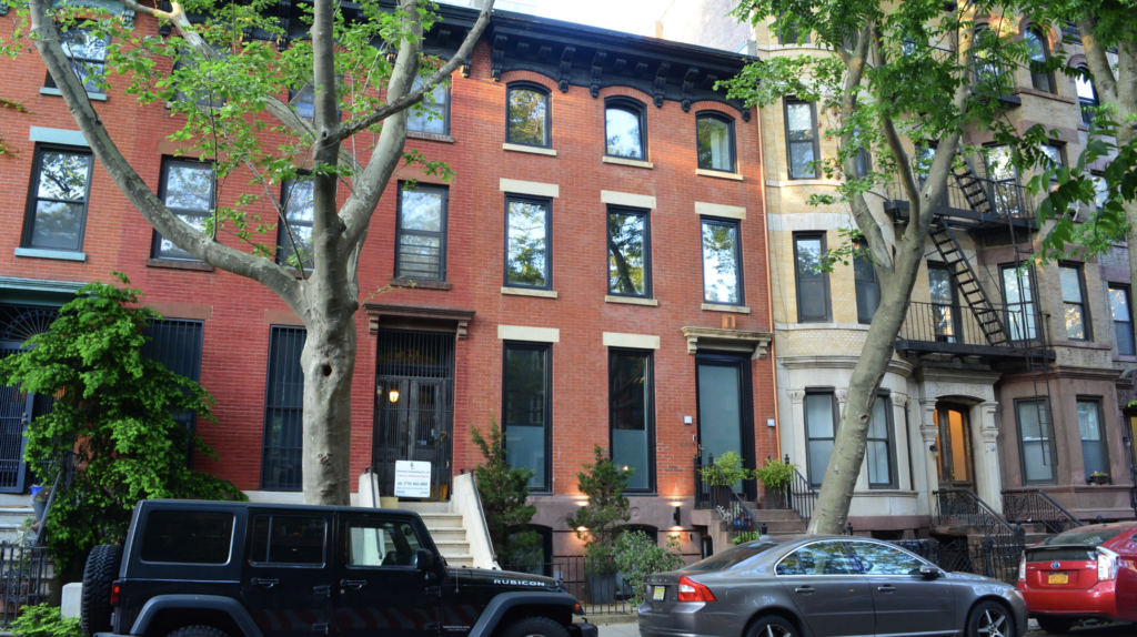 Multifamily buildings in a city with cars parked in front.