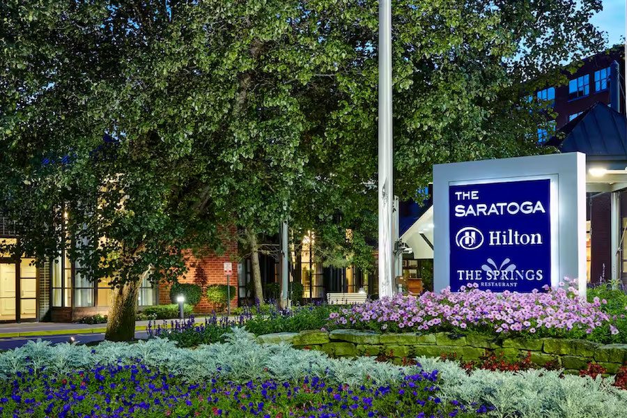 Exterior photo of the Saratoga Hilton in the evening. Flowers and lush landscaping fill the scene.