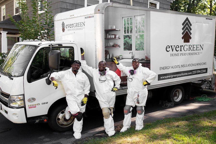 Three workers stand in front of a truck wearing white PPE.