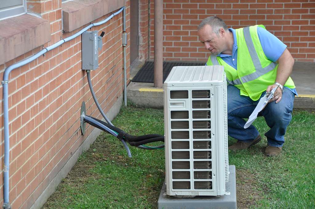 inspector with vest kneeling outside near heat pump