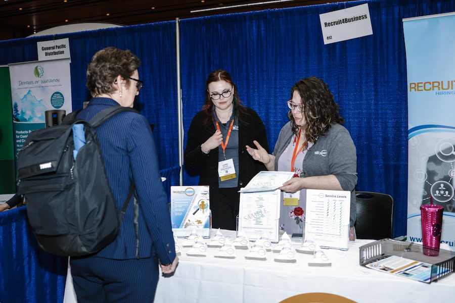 Two women at a a trade show booth speaking to an attendee