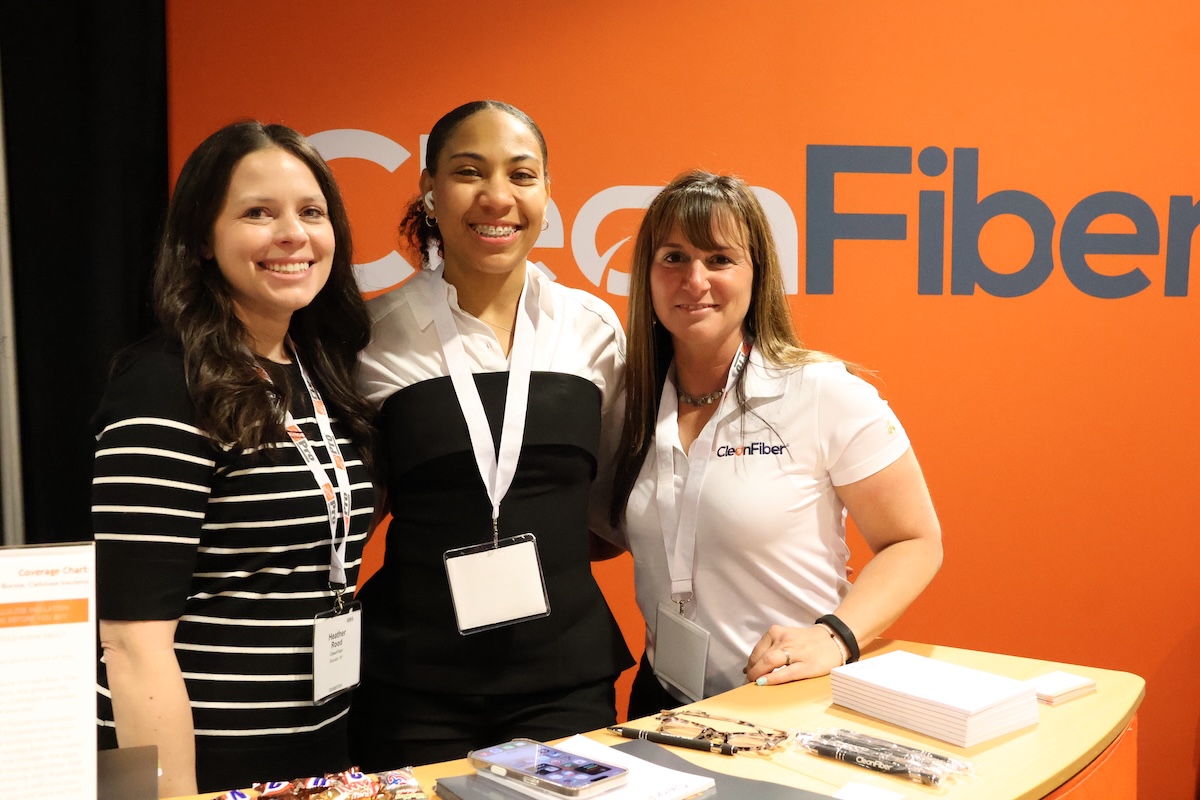 Three women pose in front of a Clean Fiber booth