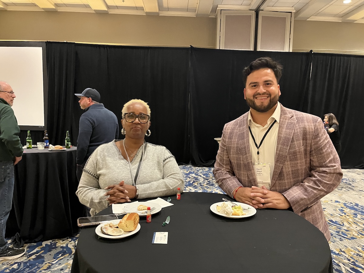 Two people standing at a tall table smiling, taken at BPA's 2025 New England Regional Home Performance Conference and Trade Show